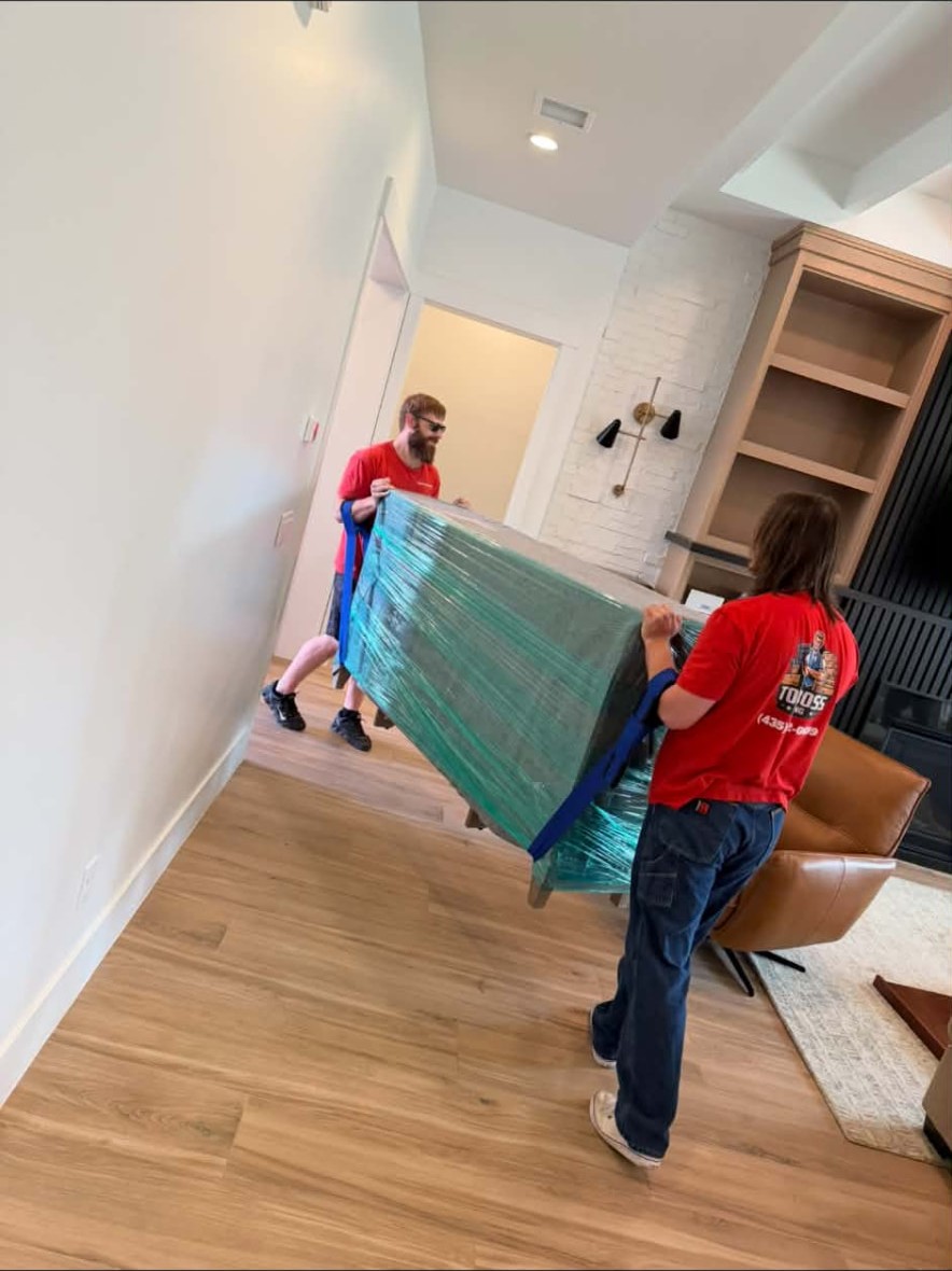 Top Boss movers carrying a shrink-wrapped sofa through a home